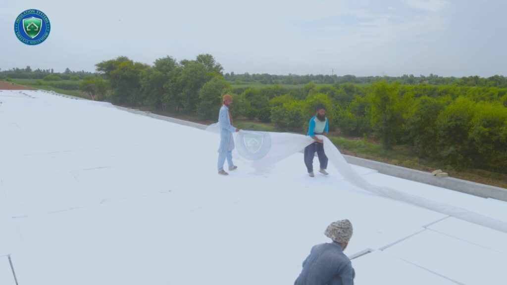Workers applying roof insulation and waterproofing treatment on a white roof